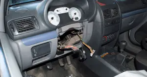 Gray interior of the car missing a steering wheel and steering column with loose wires hanging out