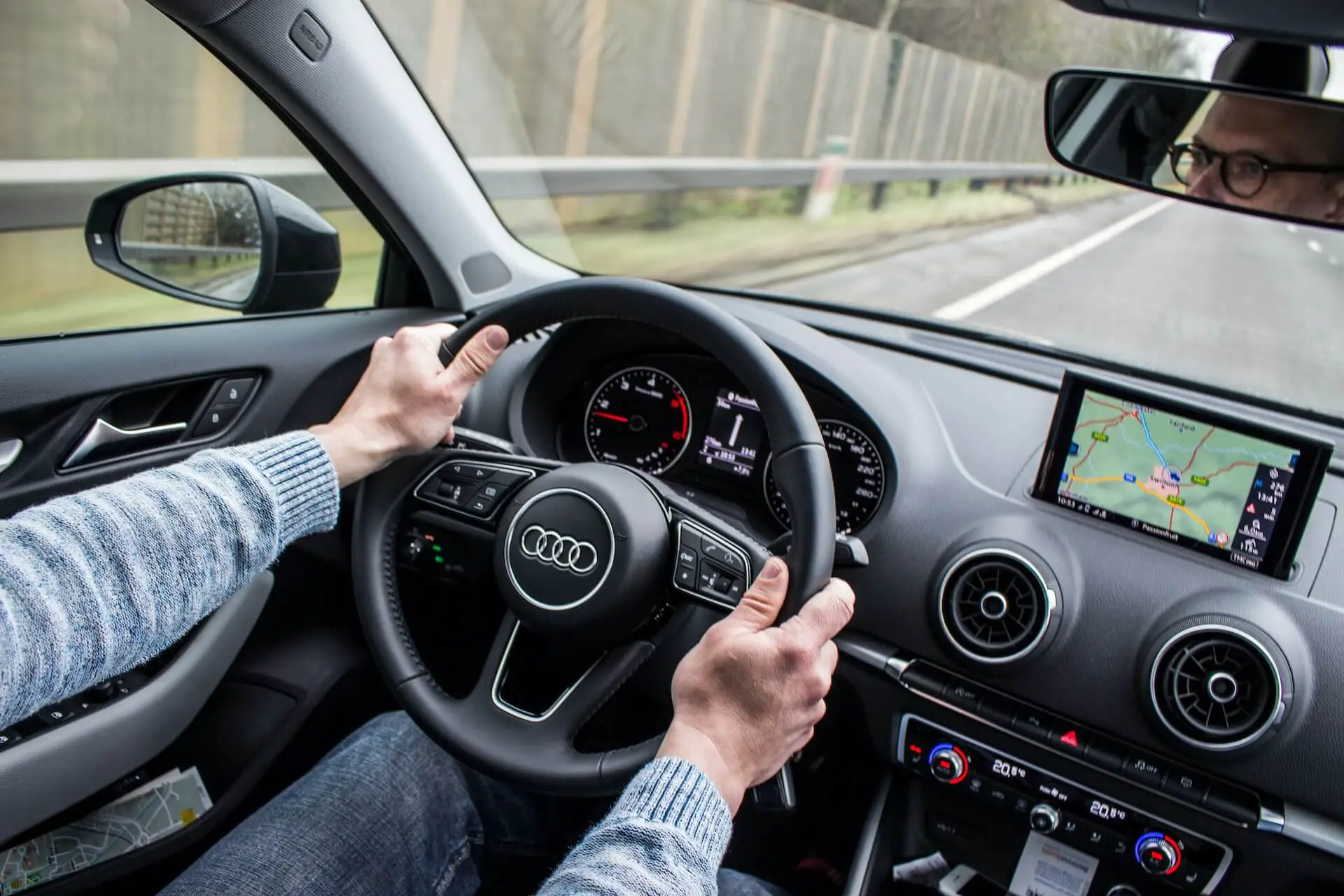 man with glasses gripping Audi steering wheel inside of car